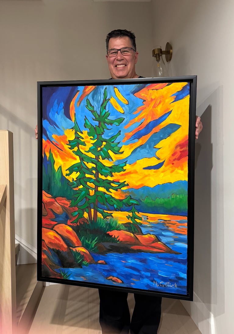 Mitch Gillick holding a painting of a Muskoka sunset
