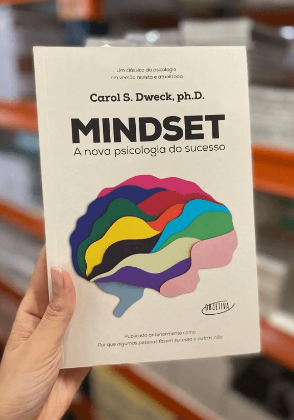 Hand holding the book Mindset by Carol S. Dweck in Portuguese, featuring a colorful brain illustration.