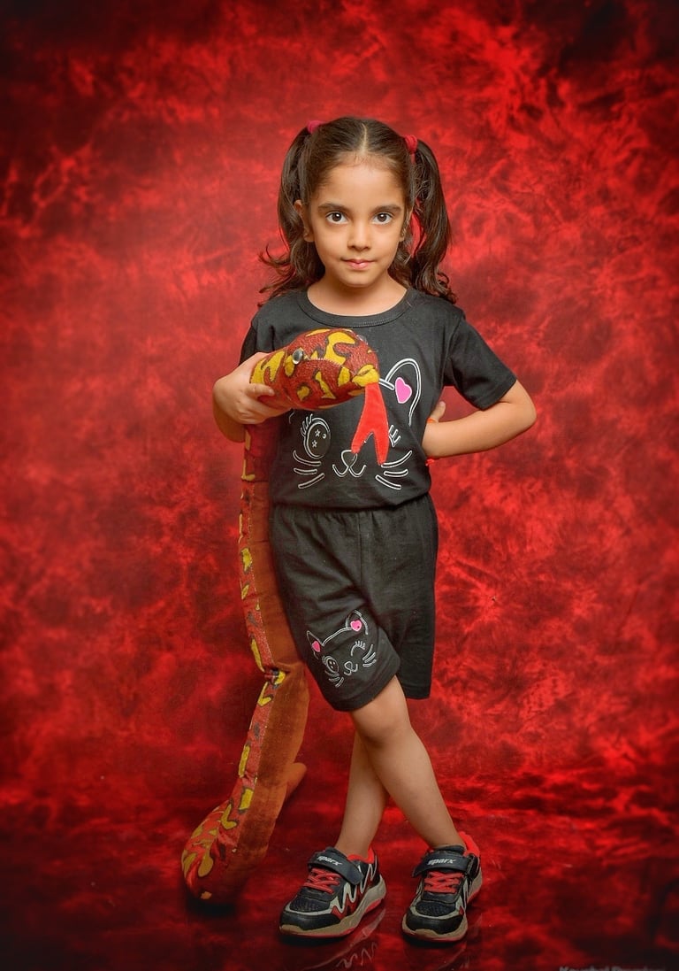 Young girl in black outfit holding a plush snake toy against a red studio background.