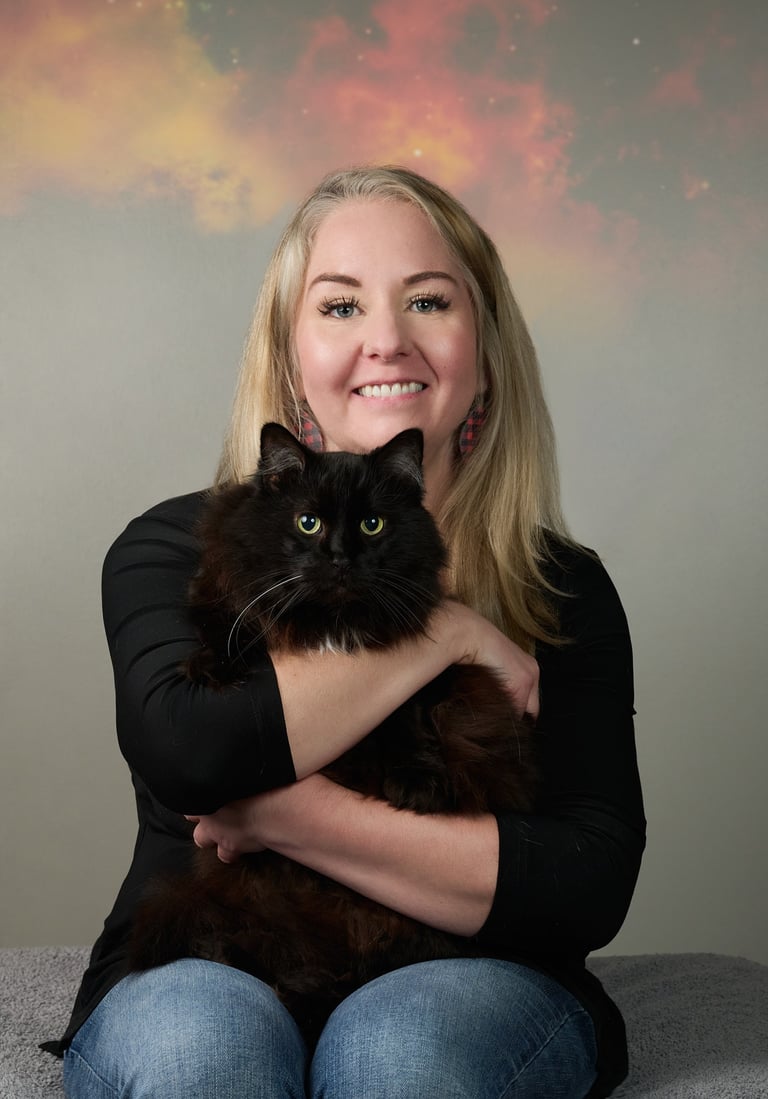 A smiling blonde woman holding a fluffy black long-haired cat in a studio portrait with a galaxy background.