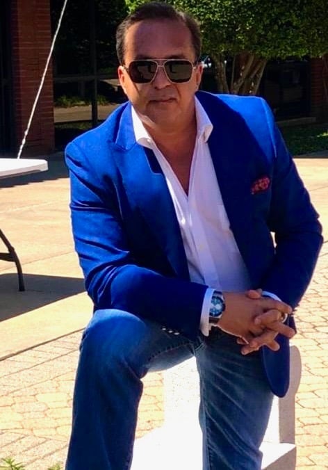 Bedig Minassian, the brand's founder, sits on a bench in a blue suit and sunglasses