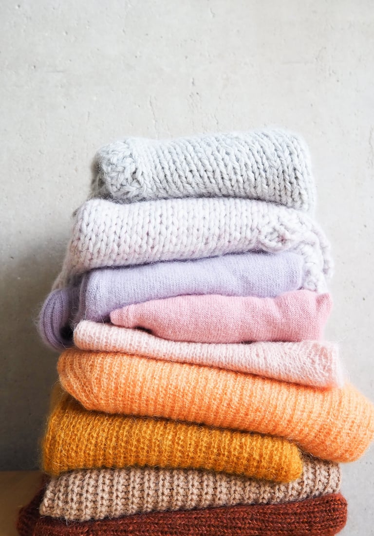 wełniane swetry ułożone w stos na tle szarej ściany