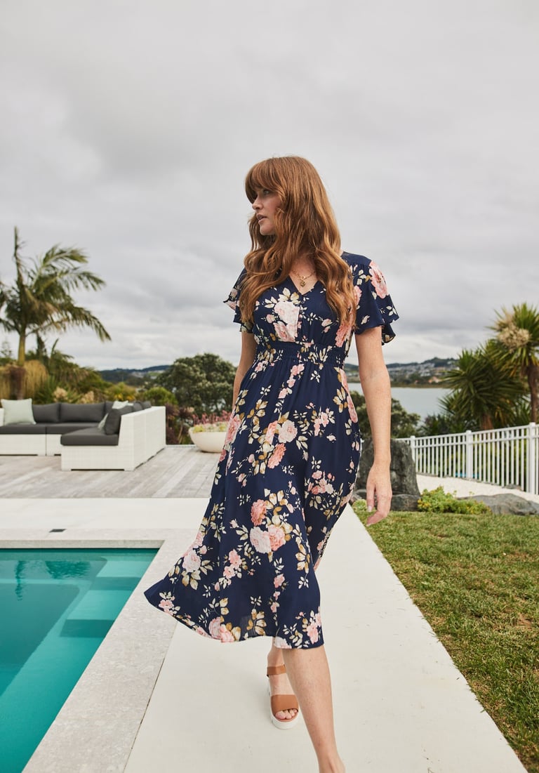 Fashion campaign photography - a woman in a floral dress standing on a patio by a pool
