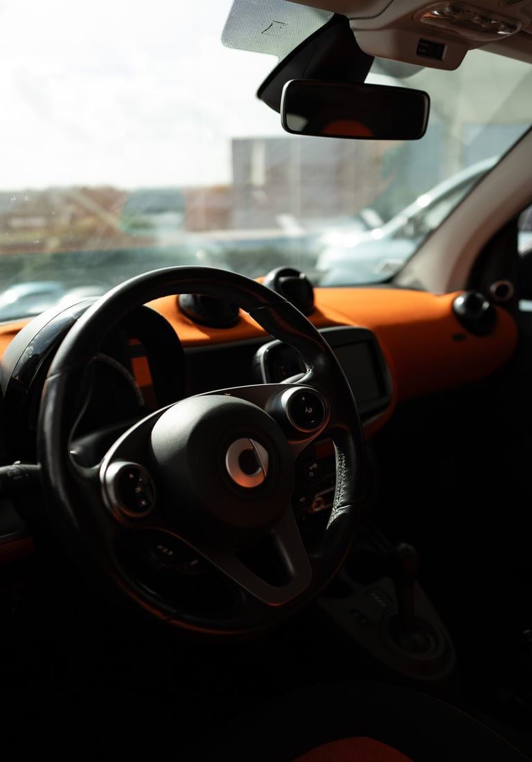 Close-up of a SMART car steering wheel and the interior of the orange dashboard, By ACAT Photos