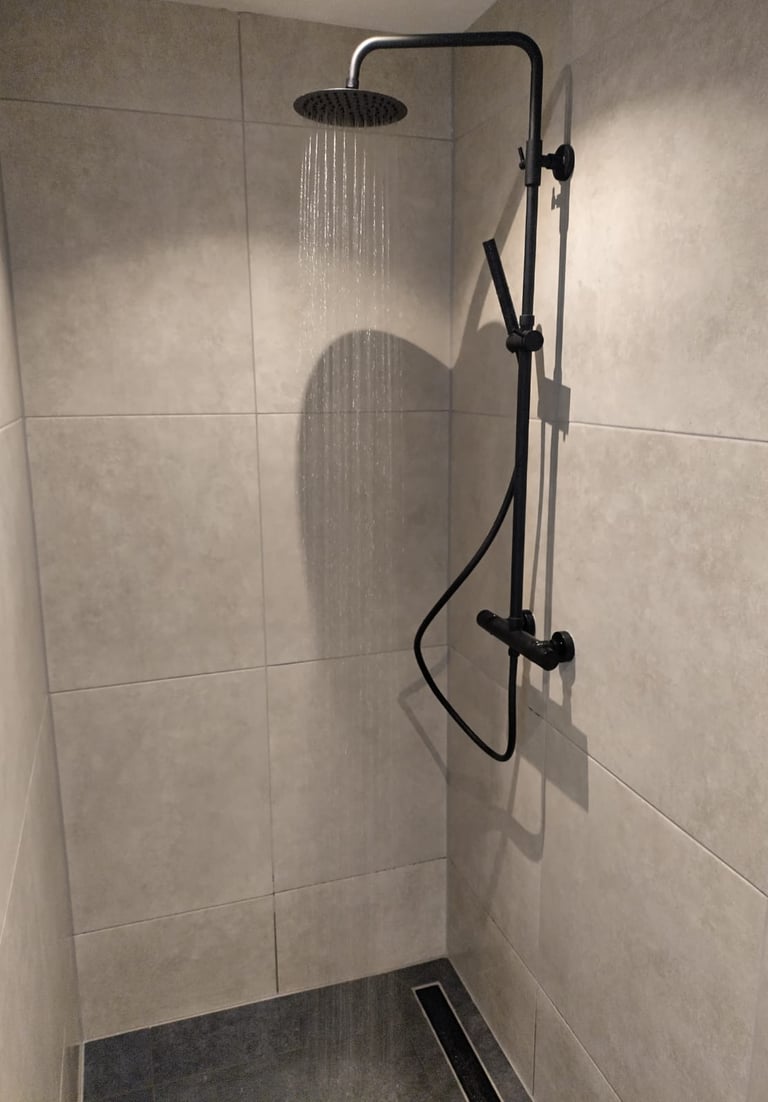 Zwarte douche in sobere badkamer met grote tegels.