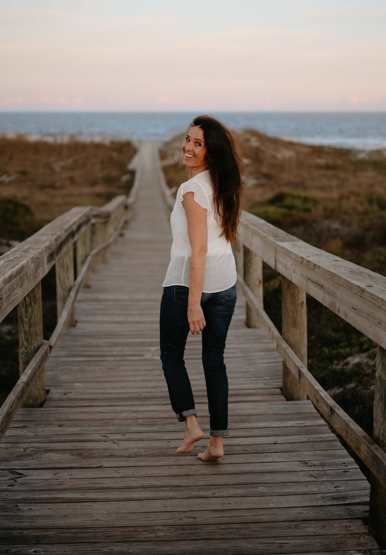 Michael Alexa Pitts walking down a wooden boardwalk over dunes toward the ocean & smiling back at you