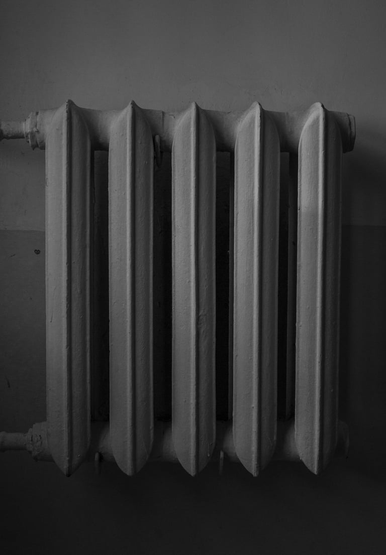 Monochrome image of a cast iron radiator against a wall.