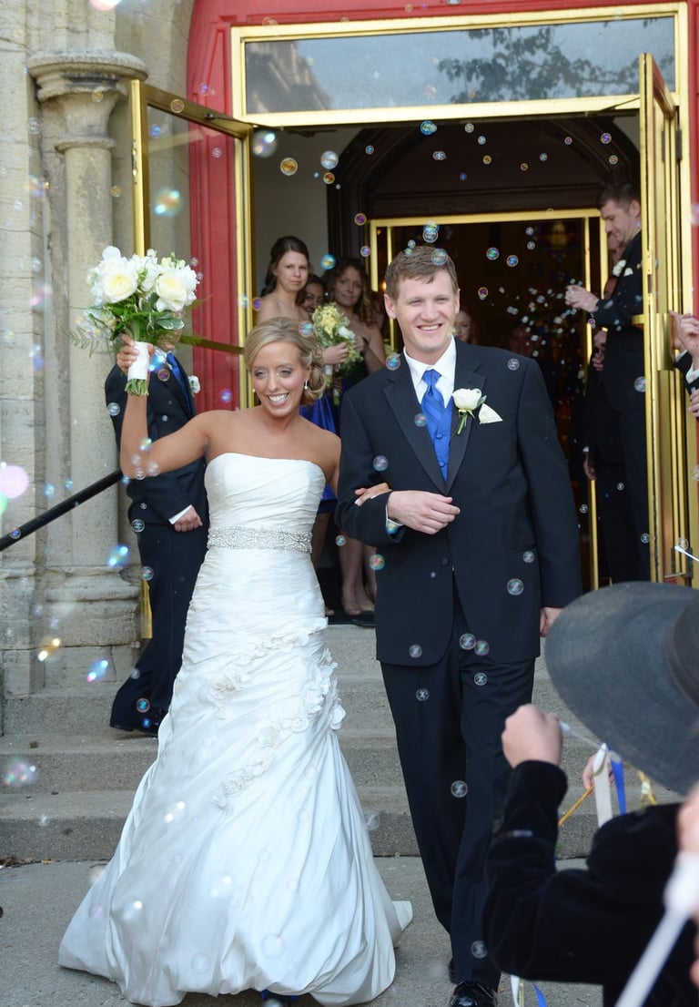 a bride and groom walking down the aisle of a wedding from church with bubbles generated by guests