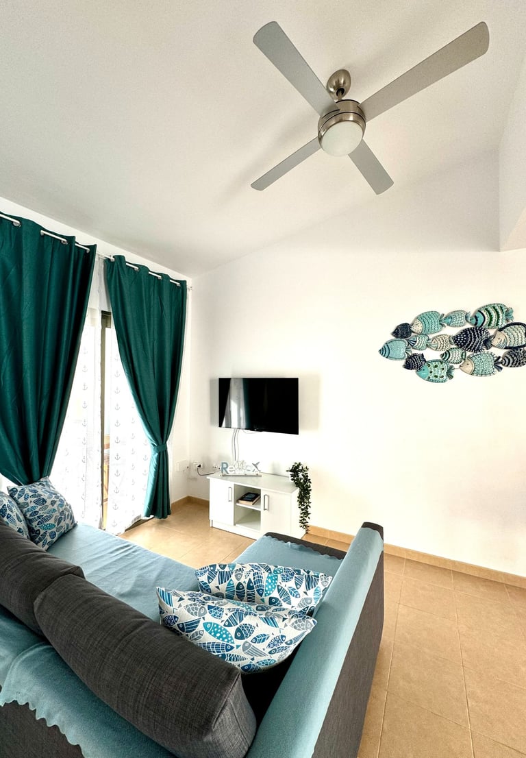Modern living room with teal curtains, a blue sofa, fish wall decor, and a ceiling fan.