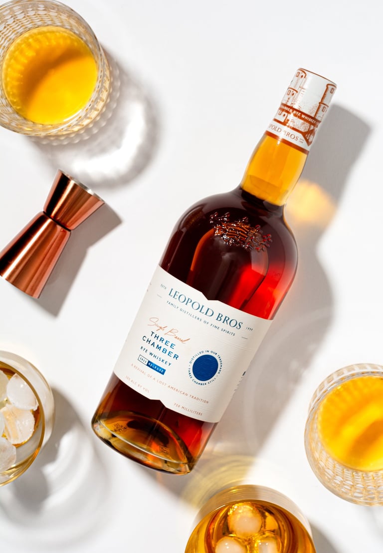 a bottle of Leopold Bros Three Chamber Rye surrounded by glasses of whiskey