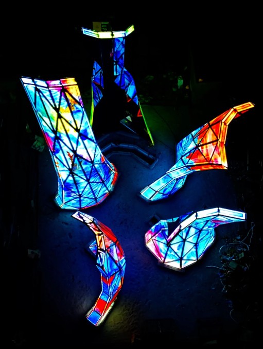 A night photo of the blooming sculpture with it's multi-colored art glass pannels illuminated