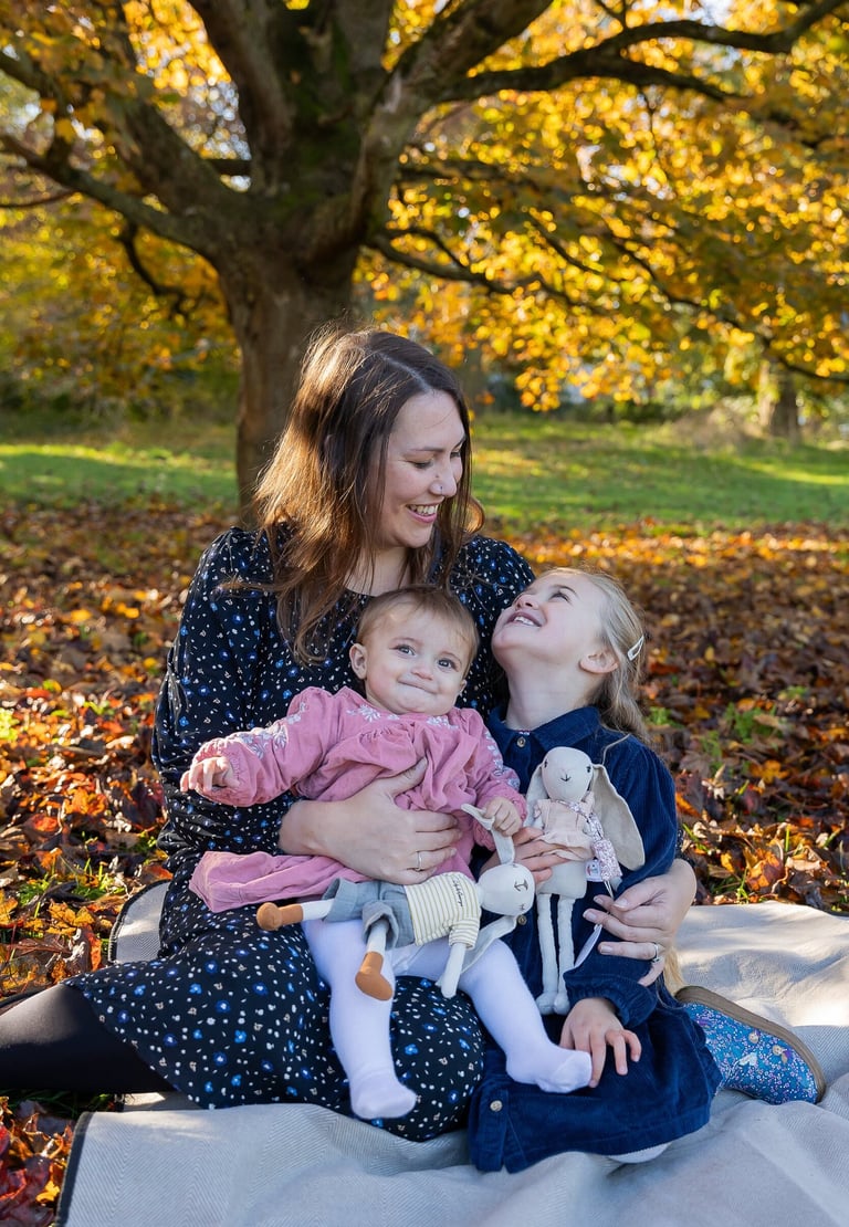 A mother and two daughters sitting on fall leaves under a golden autumn tree for a family photoshoot.