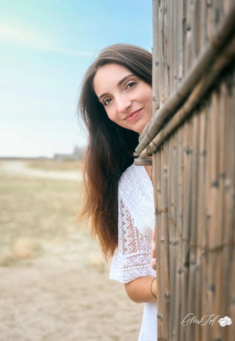 Portrait d'une femme brune souriante regardant derrière une maison de pecheur sur une plage à Canet.