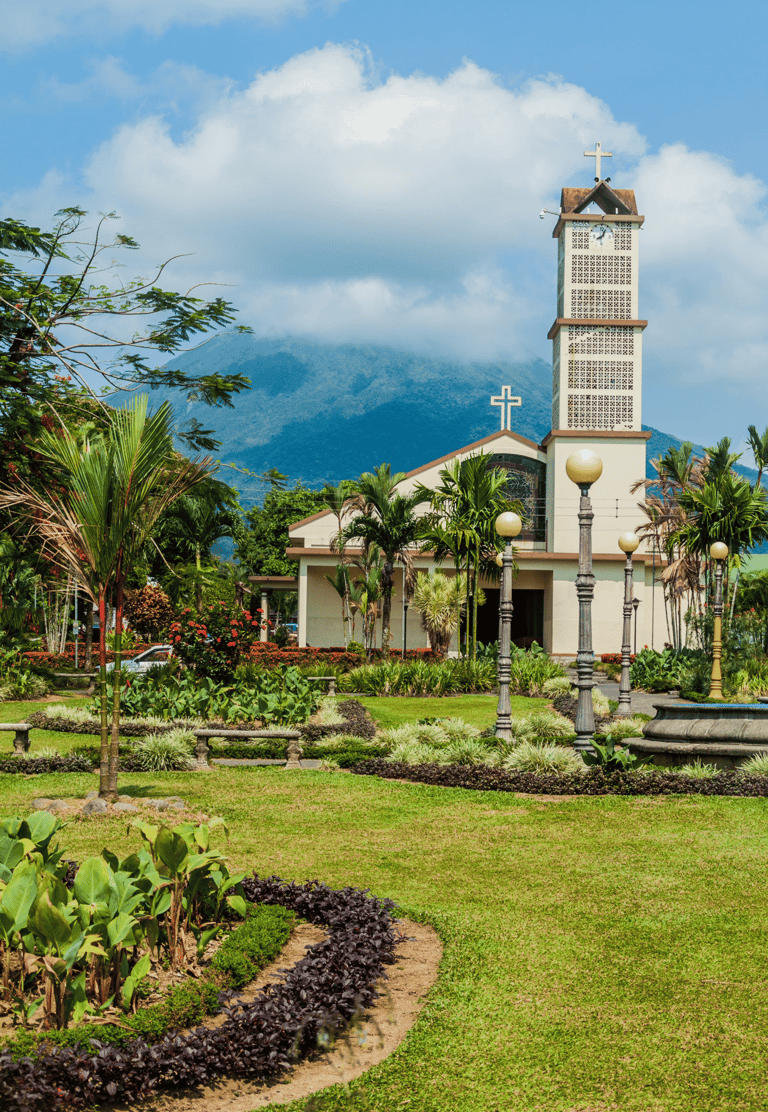 A tropical garden and church in La Fortuna with the Arenal Volcano in the background.