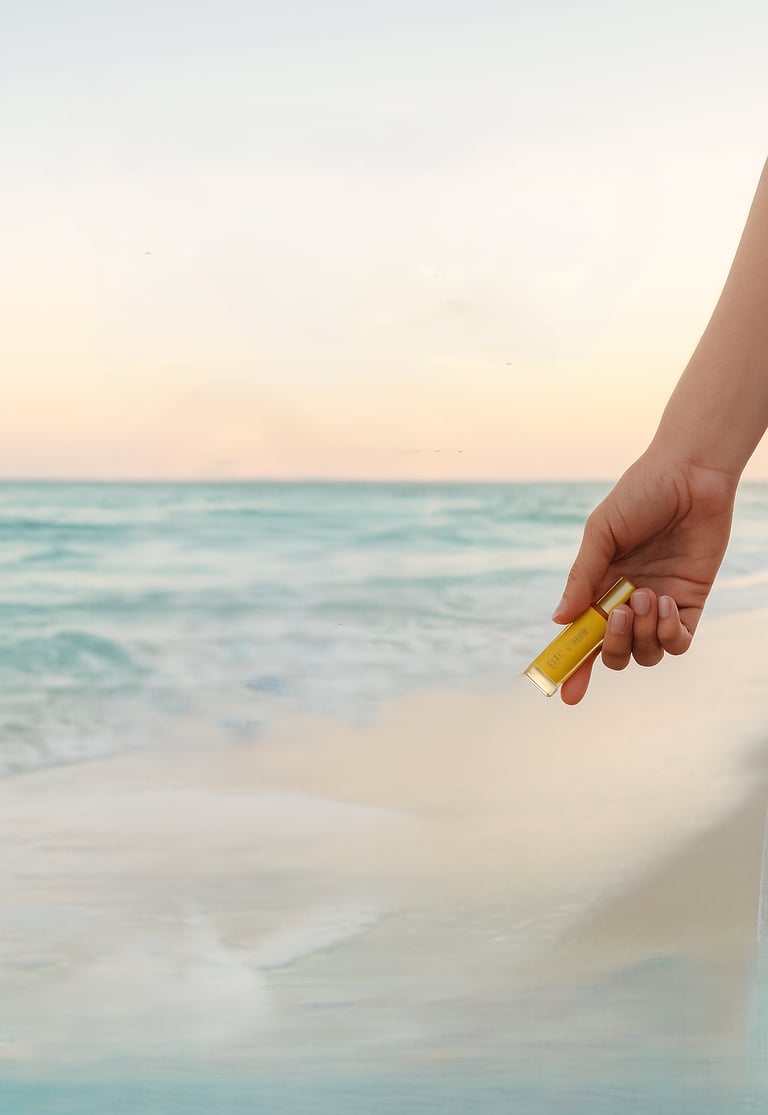 image of hand holding an essential oil bottle beachside