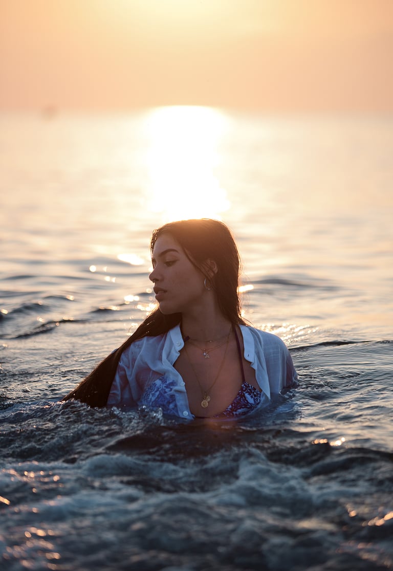 Modelo en la playa con vestido blanco y bikini a la vista, posando elegantemente