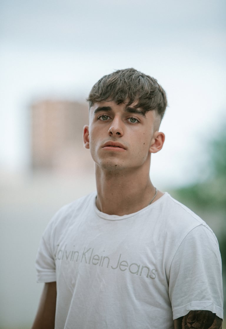 Primer plano del modelo con camiseta blanca y gafas de sol Hawkers, con Seat León rojo de fondo