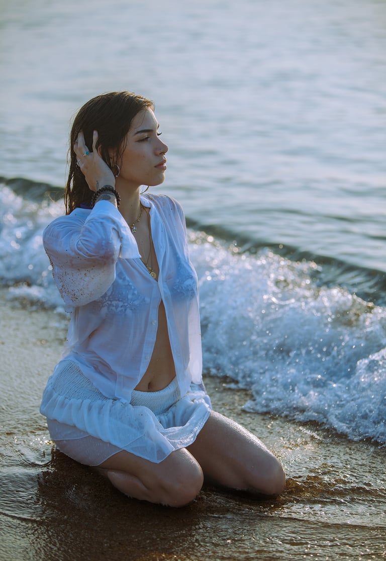 Modelo posando en la playa con un vestido blanco y un collar, fondo marino