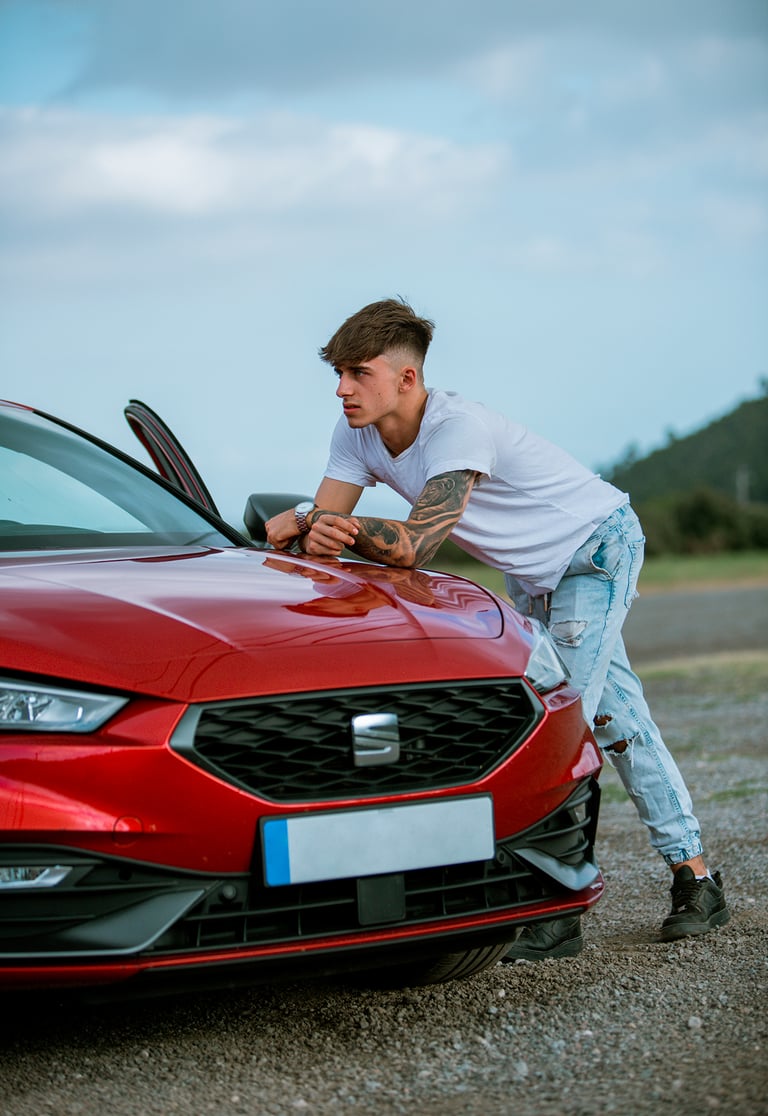 Sesión de fotos diurna con modelo en camiseta blanca junto a un Seat León rojo en un ambiente urbano