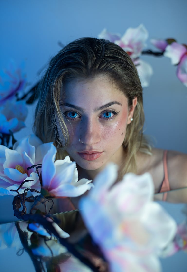 Modelo con maquillaje de sirena, reflejo de agua en espejo y decorada con flores en estudio