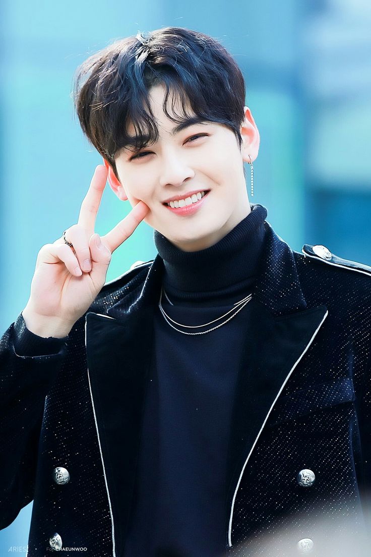 K-pop idol Cha Eun-woo smiling and making a peace sign in a black turtleneck and jacket.