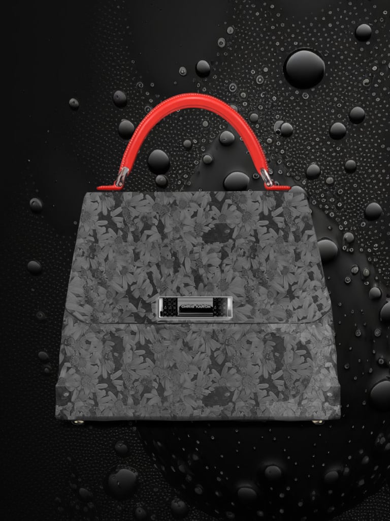 Elegant grey floral pattern designer handbag with a vibrant red handle on a water-droplet background.
