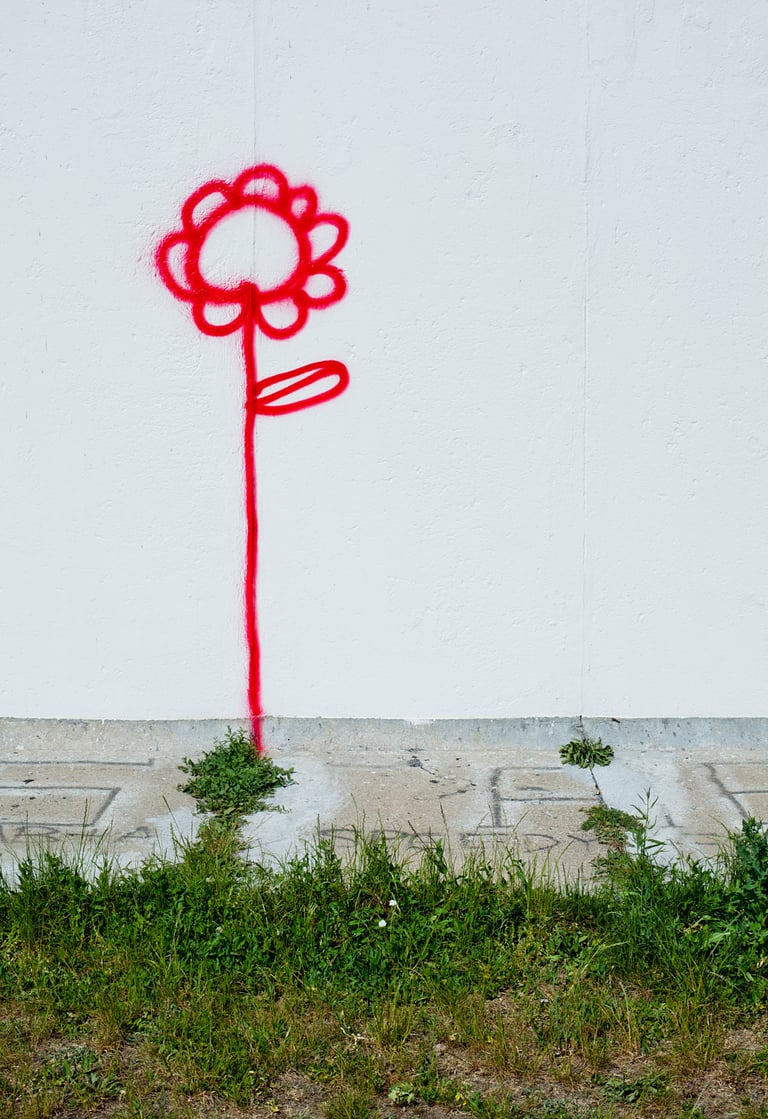 A red flower on a wall next to grass.