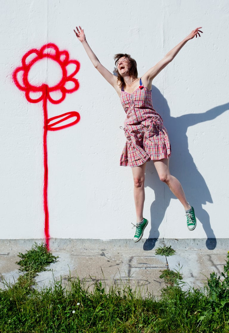Phoebe Kreutz laughing and jumping next to a wall with a flower.