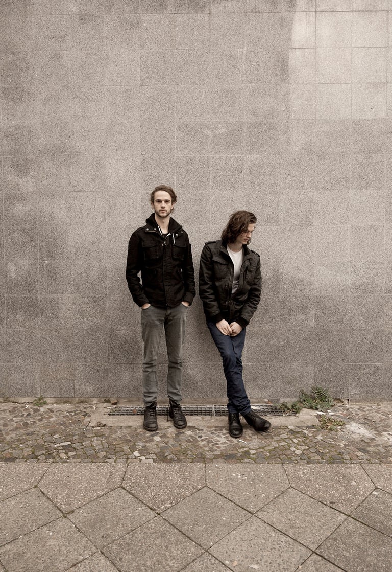 Two musicians standing against a wall.
