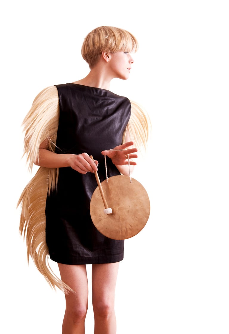 Sandra Kolstad wearing a dress with hair hitting a gong.