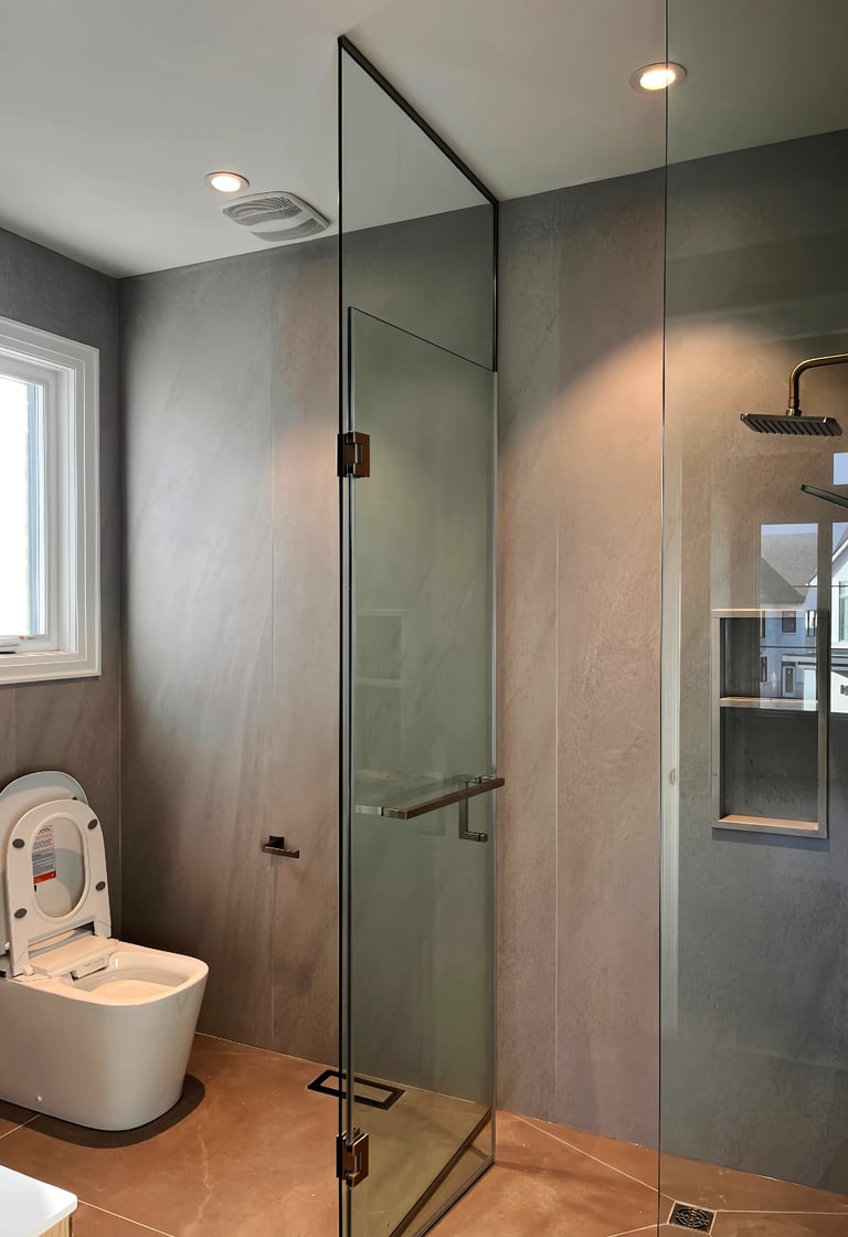 Modern bathroom with a glass walk-in shower, rain shower head, and sleek white toilet against gray tile walls.