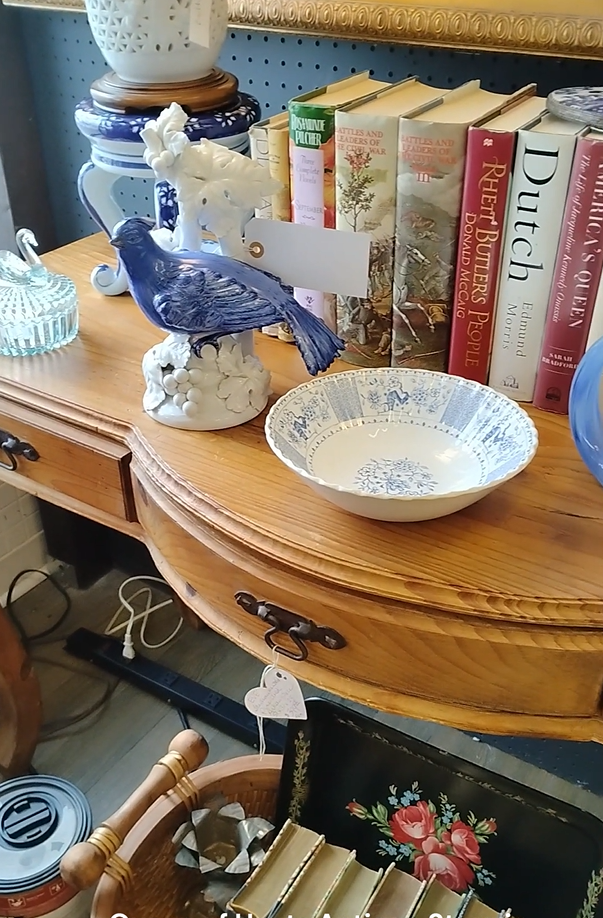 Antique store display with books, dishes, and a blue bird figurine, symbolizing old habits.