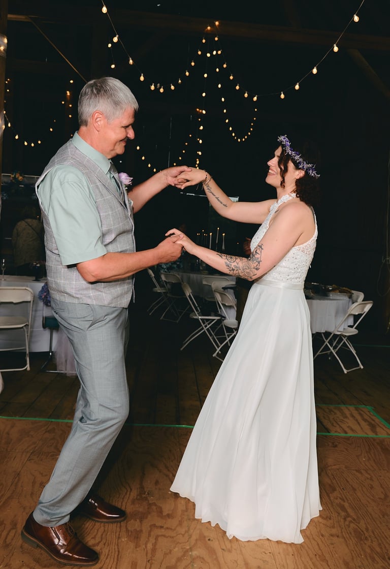a bride and her father dancing at a wedding in a barn
