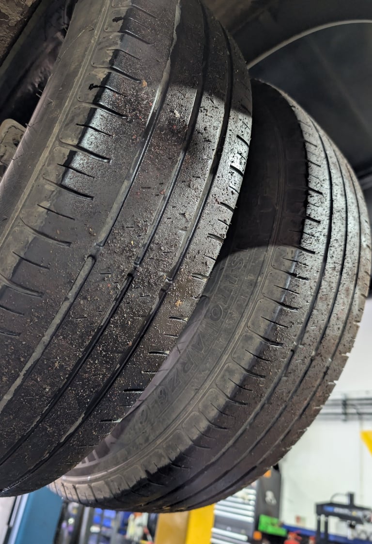 Close-up of worn car tires with uneven tread wear hanging on a vehicle lift in an auto repair shop.