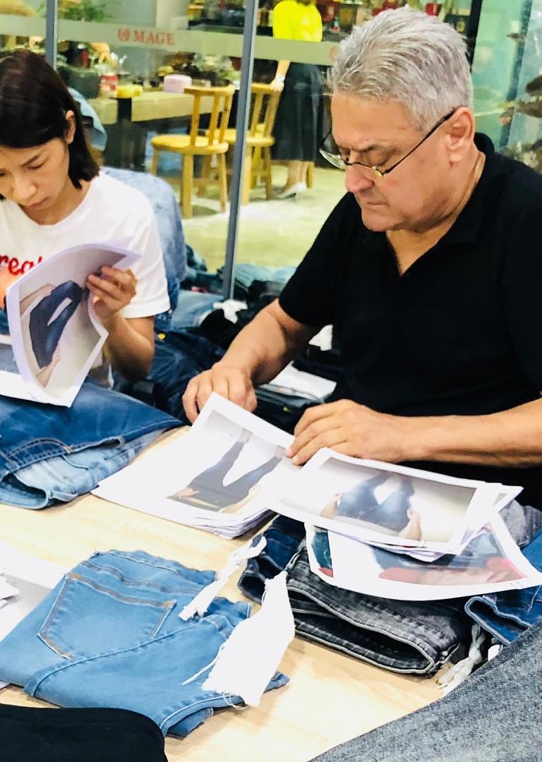 Fashion designers reviewing denim samples and product photos at a workstation for apparel manufacturing.
