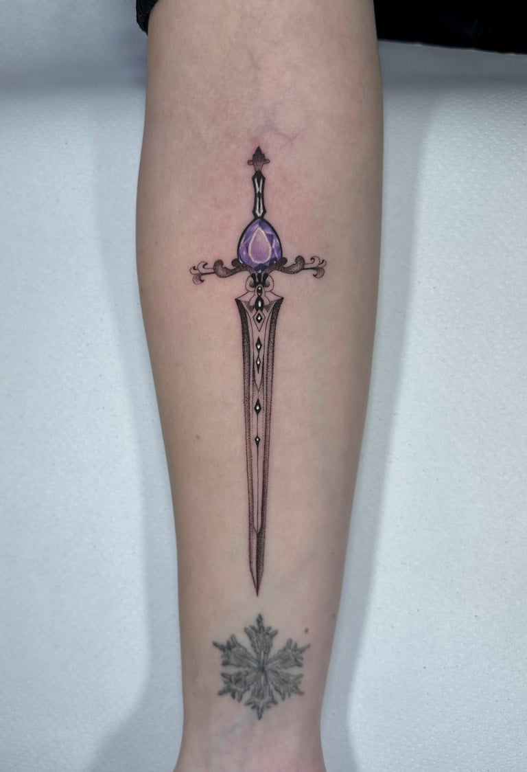 Tatuaje fineline en Madrid de espada ornamental con gema morada empuñadura decorada