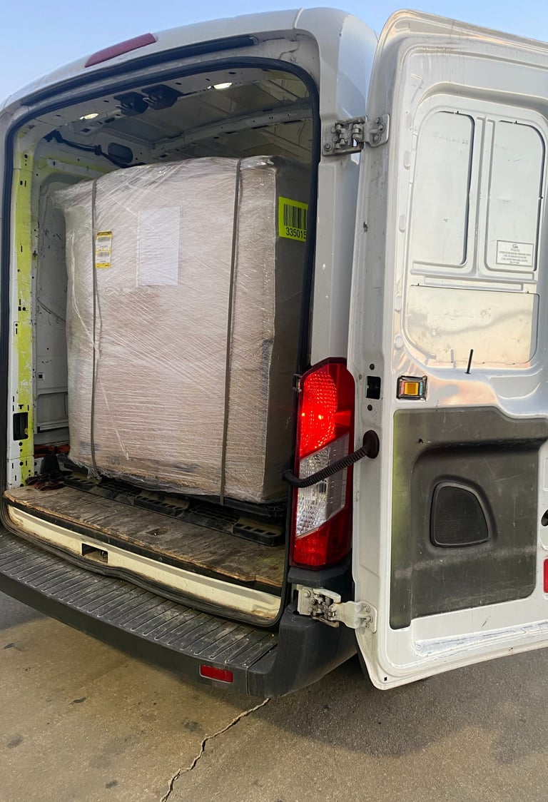 Rear view of a white delivery van with its rear doors open showing a large shrink-wrapped pallet