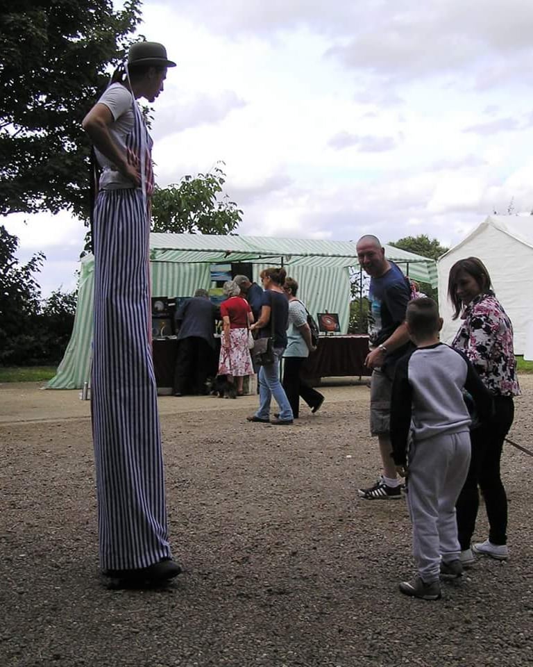 A circus entertainer on stilts wearing striped trousers performs for a crowd at an outdoor community festival.