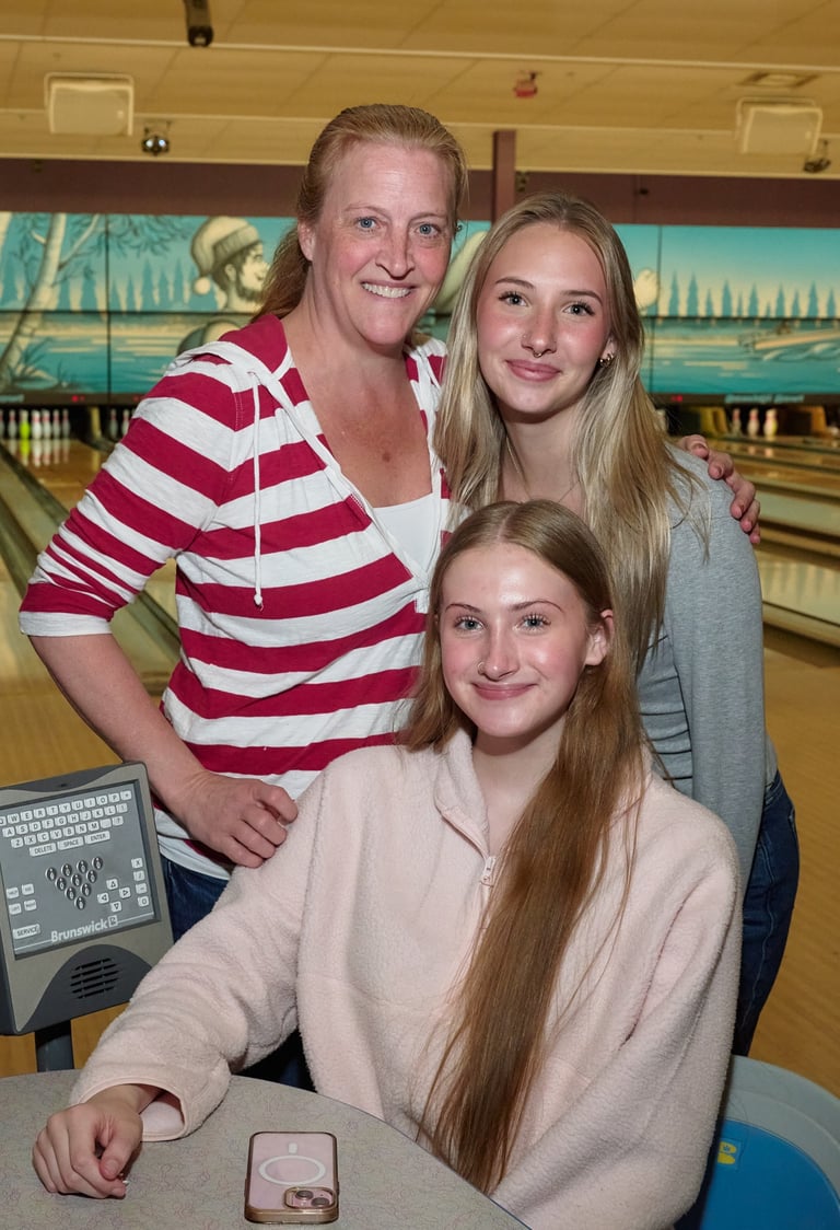 A smiling mother and her two teenage daughters posing together at a bowling alley.