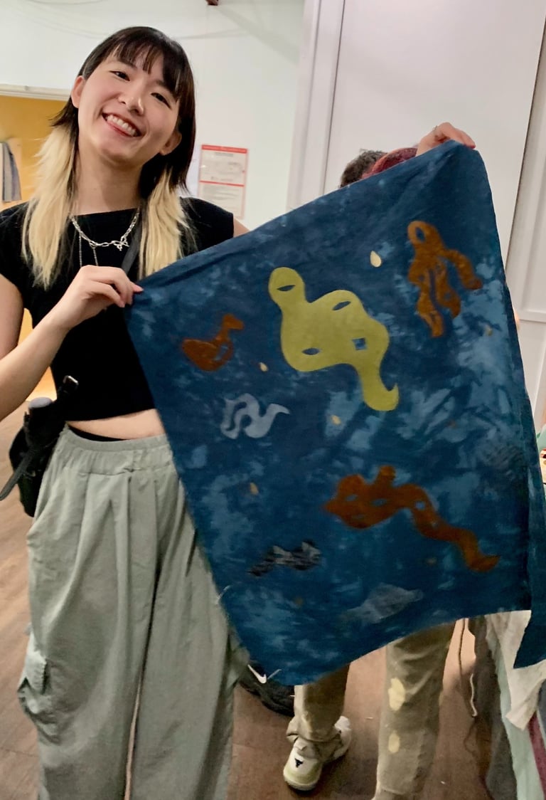 A person with blonde and black hair and light skin holds a banner smiling.