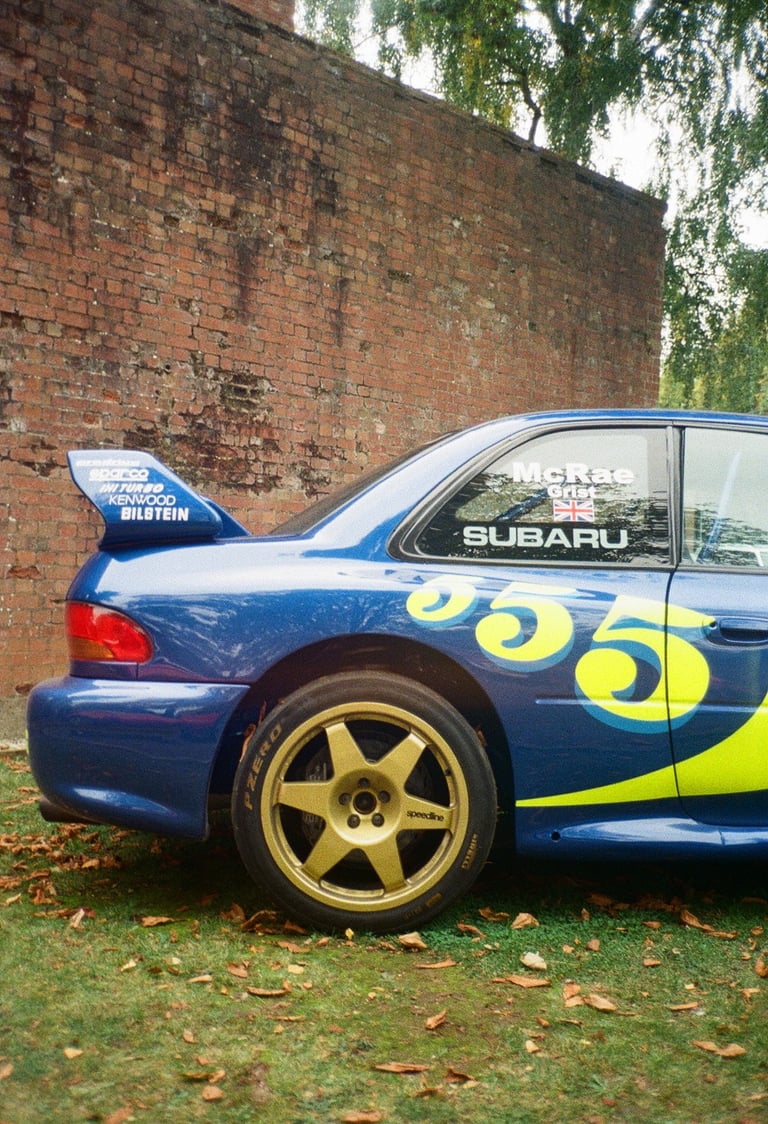 a Subaru Impreza rally car parked in front of a brick building