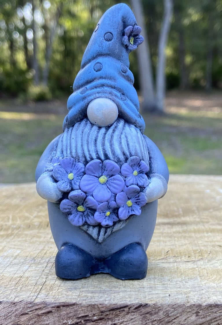 A concrete garden gnome figurine holding a bouquet flowers.