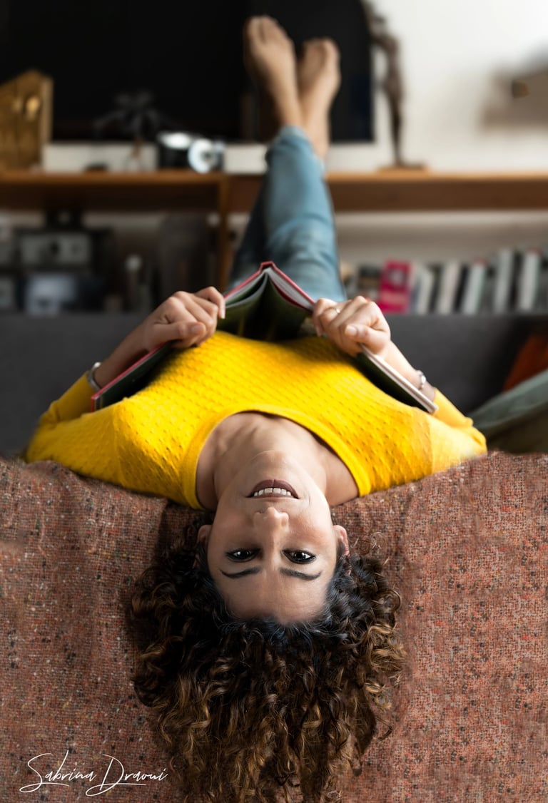 a corporate woman upside down laying on a couch with a book 