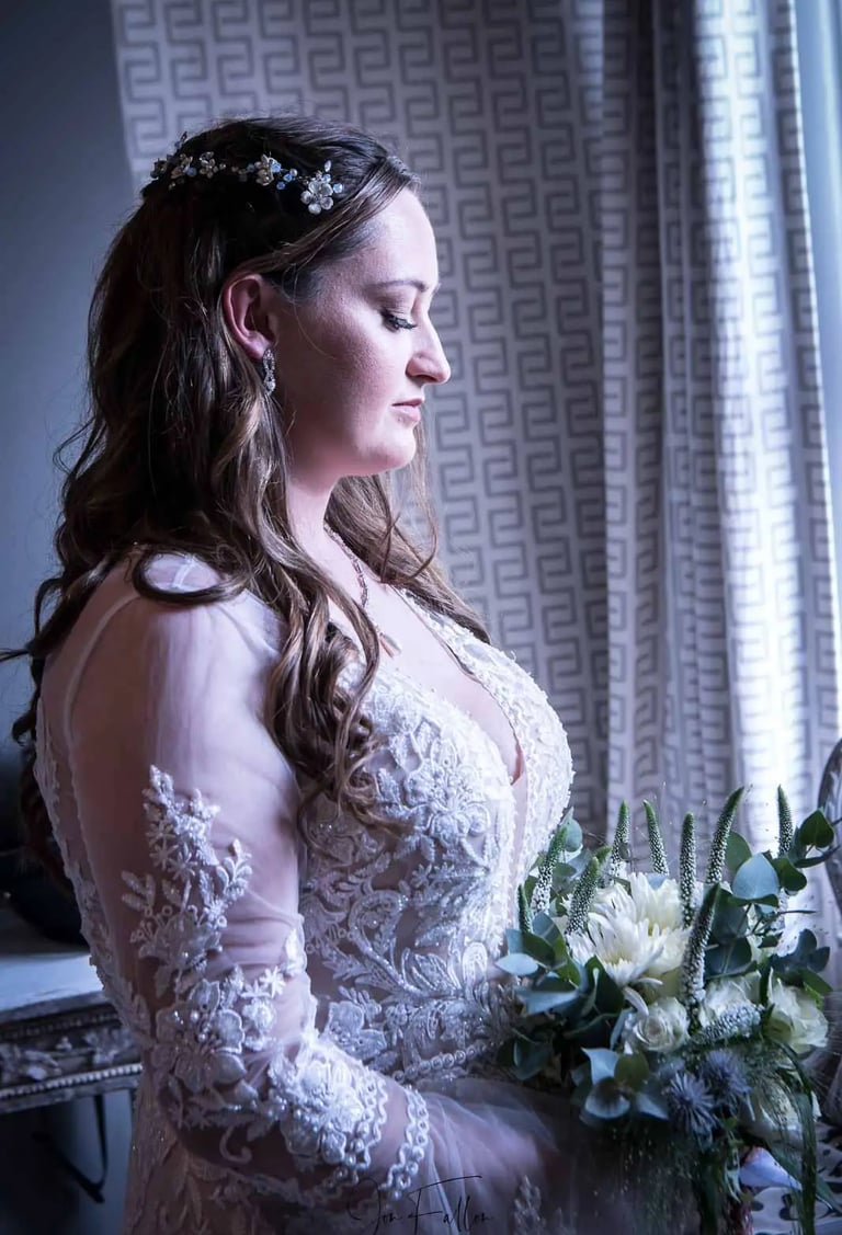 Side profile of a bride in an embroidered lace wedding dress holding a white floral bouquet.