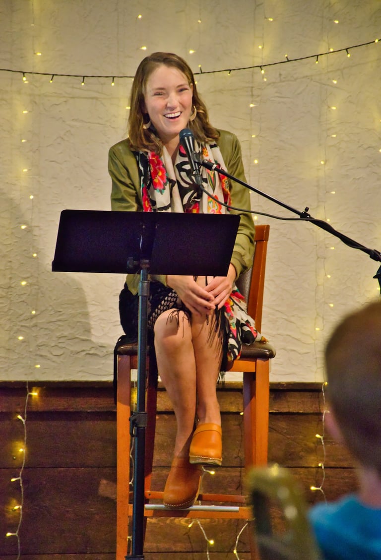 a woman sitting in a chair with a microphone smiling at the audience