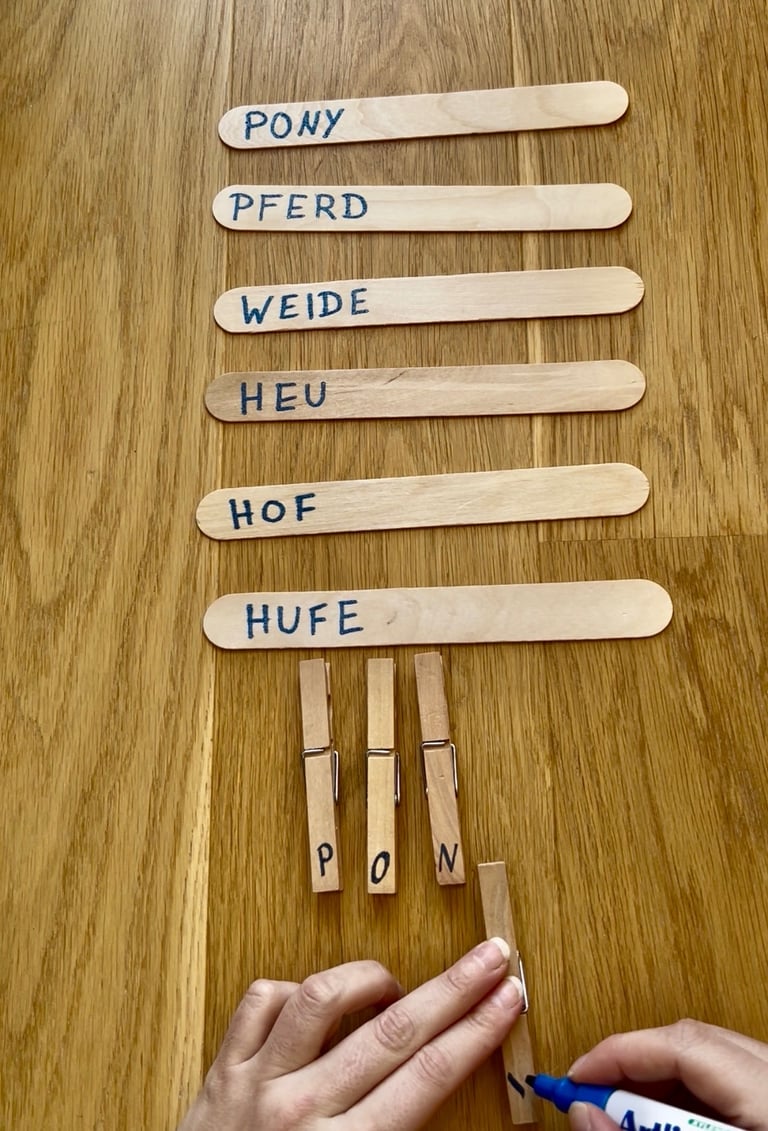 Handwriting German horse-themed words on wooden craft sticks and clothespins for a literacy activity.