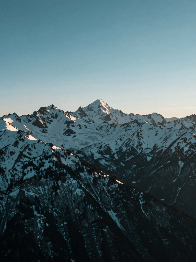 A wide-angle landscape photograph of a snow-capped mountain range in North America under a steel blue morning sky. The lighting is crisp and clear, emphasizing the rugged peaks and the serene atmosphere. The style is modern and minimalist, with a deep teal and muted green palette reflecting the pristine wilderness.