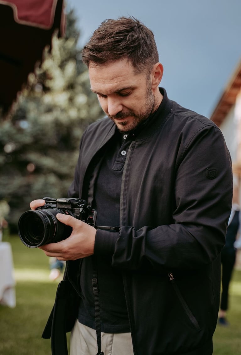 Professional male photographer in a black jacket reviewing photos on a digital mirrorless camera outdoors.
