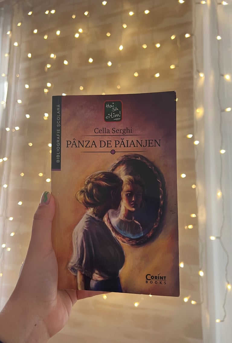 Mână ținând cartea 'Panza de paianjen' de Cella Serghi pe un fundal de luminițe de basm.