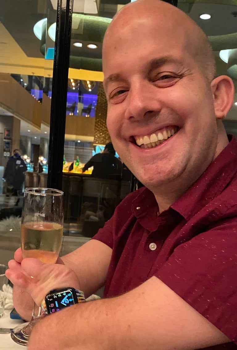 Yoav Rokach Penn wearing a red dress shirt, in a restaurant holding a Champaign glass.